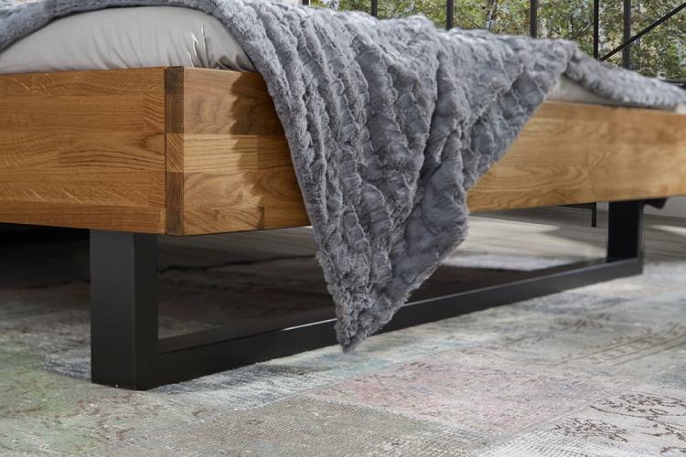 Detal łóżka dębowego FADO, ukazujący połączenie ramy z naturalnego dębu z czarnymi metalowymi płozami, widoczny fragment narzuty, nowoczesny styl loft, do sypialni.