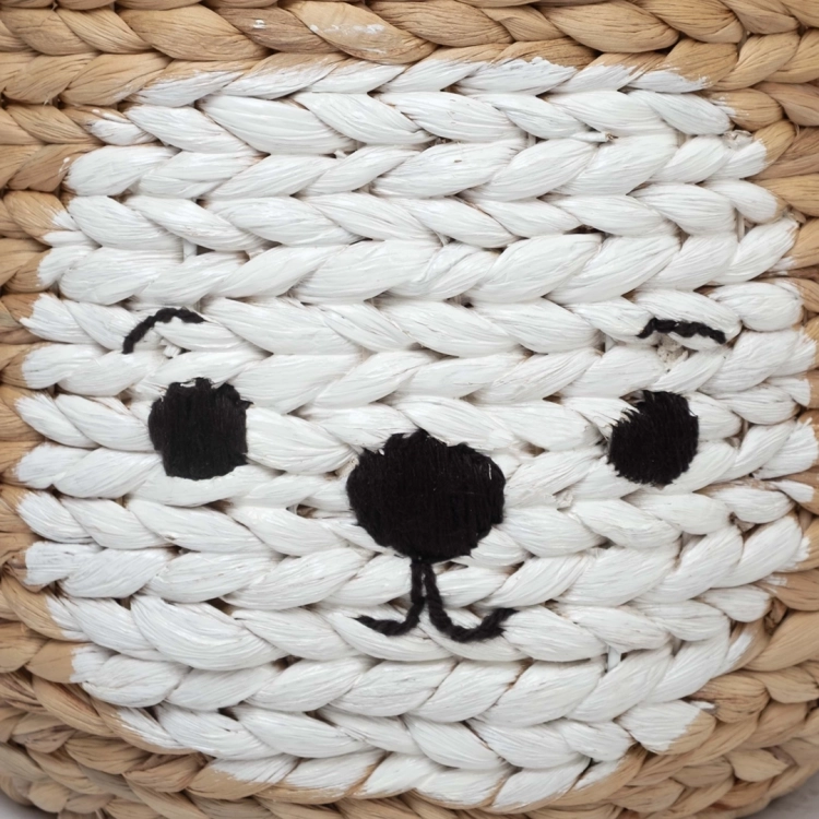 Zbliżenie na ręcznie malowaną buźkę zwierzątka na brązowym koszu na zabawki plecionym z hiacyntu wodnego.