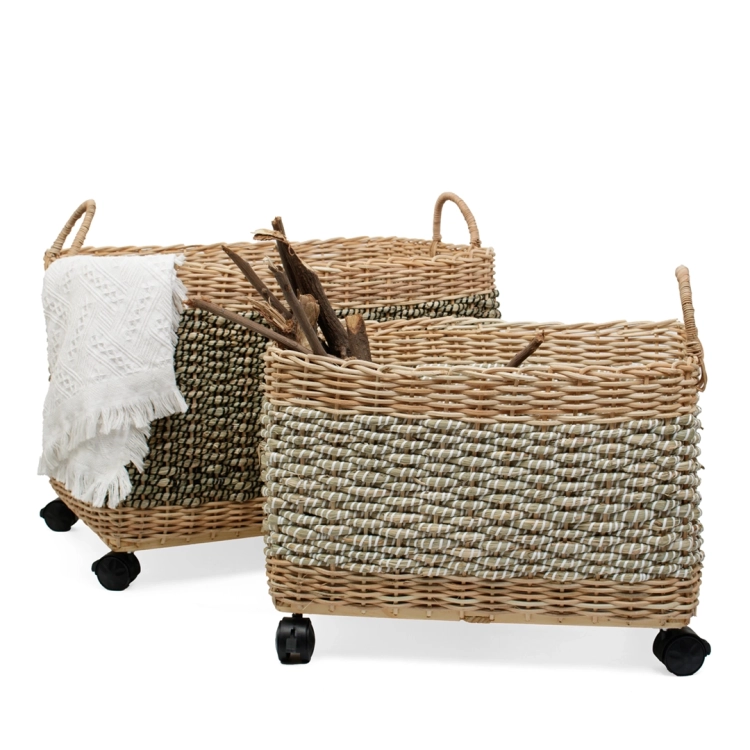 Dwa prostokątne kosze plecione z trawy morskiej na kółkach z dekoracyjnym białym kocem i drewnem.