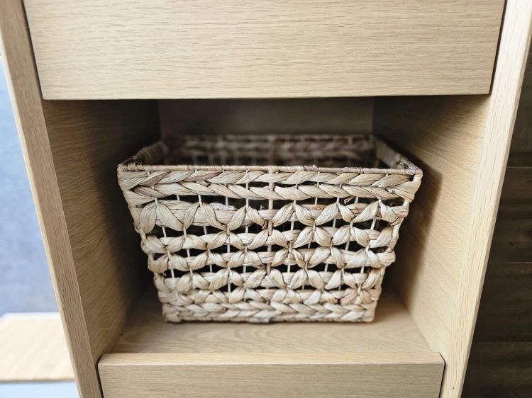 Prostokątny kosz pleciony z naturalnego hiacyntu wodnego w stylu boho, umieszczony w jasnej, drewnianej półce regału. Widoczny gruby, ozdobny splot materiału w odcieniach brązu.