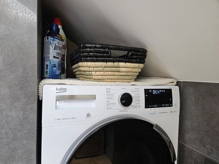 Prostokątny kosz pleciony z naturalnej trawy morskiej i hiacyntu w kolorze czarno-brązowym, ustawiony na pralce.