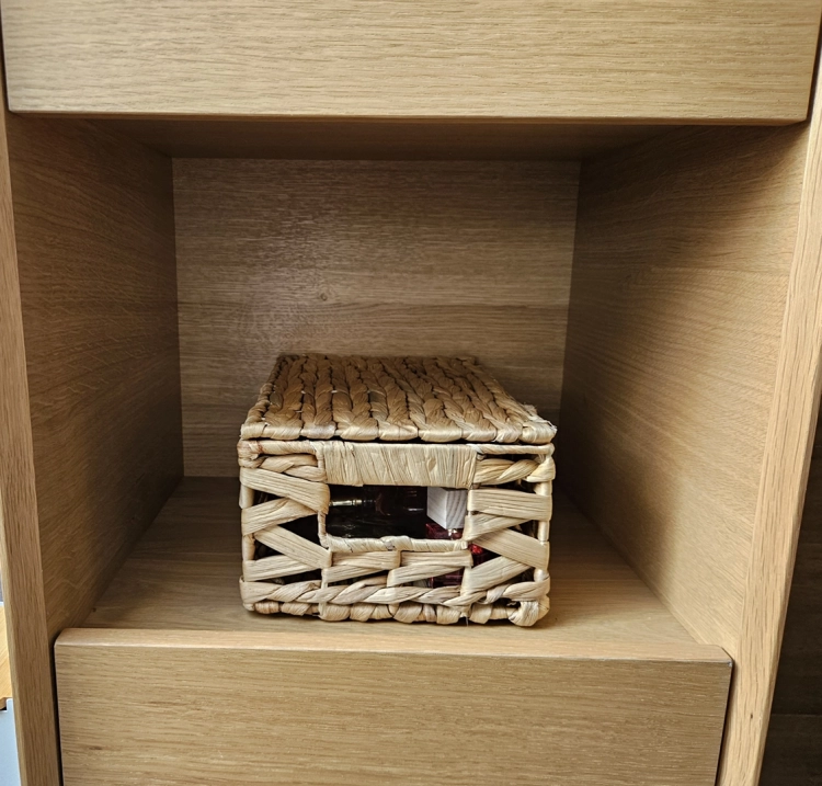 Zamykany kosz pleciony z hiacyntu wodnego wewnątrz jasnej, drewnianej szafki. Ozdobny pojemnik do przechowywania w stylu rustykalnym z widocznym uchwytem.