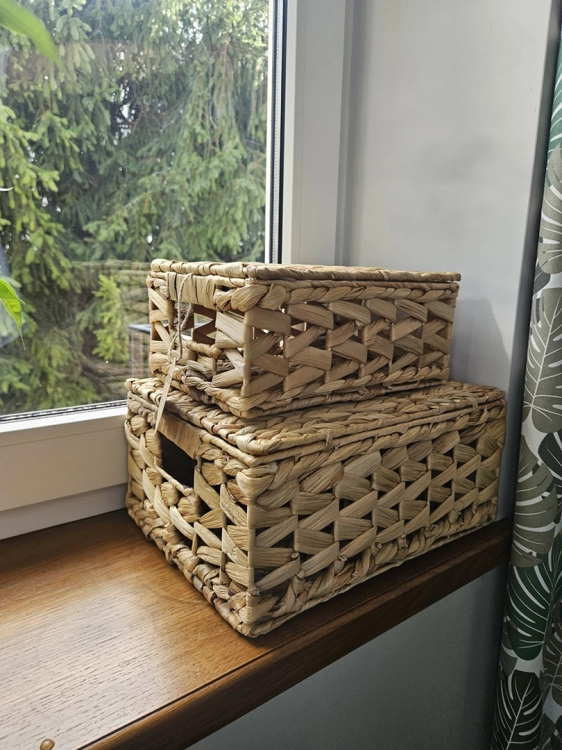 Zamykane kosze dekoracyjne z hiacyntu wodnego w stylu boho. Plecione pudełka do przechowywania z grubym splotem, stojące na parapecie przy oknie. Ekologiczny dodatek do wnętrz