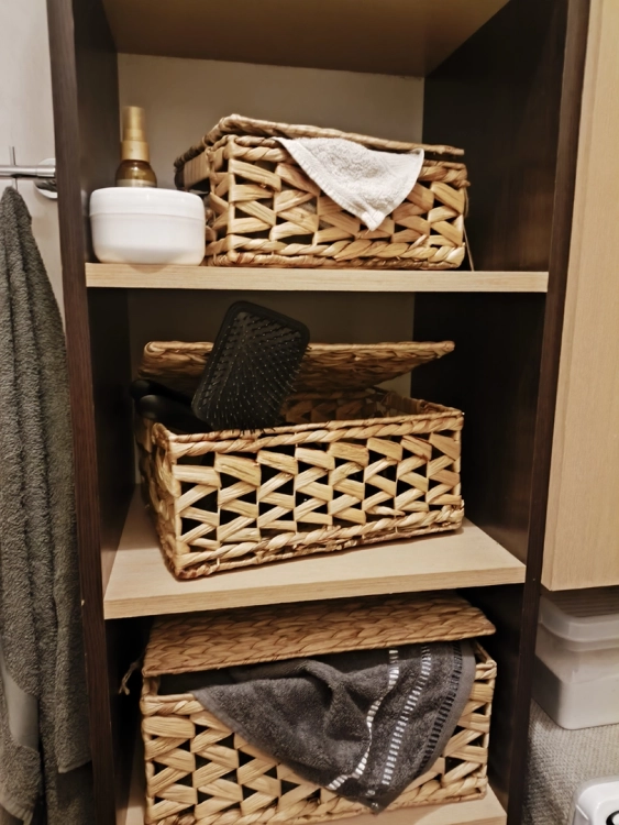 Plecione kosze z hiacyntu wodnego z pokrywką na ciemnym regale w łazience. Wewnątrz ręczniki i akcesoria. Naturalny pojemnik do przechowywania z wyściółką.
