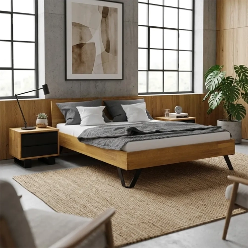Aranzacja nowoczesnej sypialni w stylu industrialnym. Centralnym punktem jest łóżko Toro Classic 140x200 cm wykonane z litego dębu, obok którego stoi dopasowana szafka Vigo. Wnętrze dopełniają betonowa ściana, duże okna, jutowy dywan i zielona monstera.
