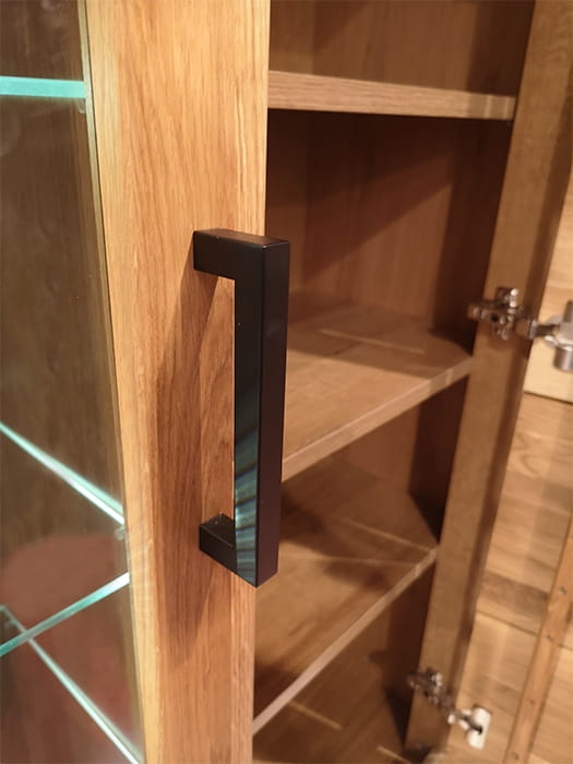 Otwarta witryna dębowa Como 2, prezentująca przeszkloną część z trzema półkami szklanymi i oświetleniem, oraz obok otwartą szafkę z trzema solidnymi, drewnianymi półkami, naturalny dąb.